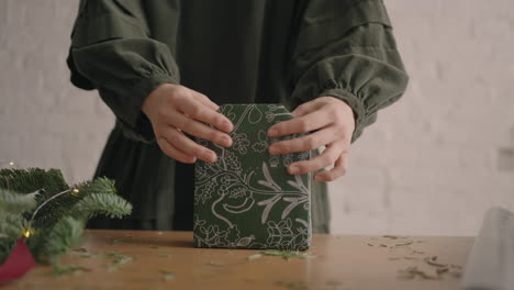 una mujer en una mesa de madera decora un regalo de navidad verde