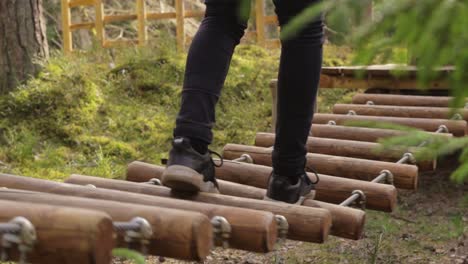 Person-walking-over-dangerous-suspension-bridge-made-of-wood,-low-leg-shot