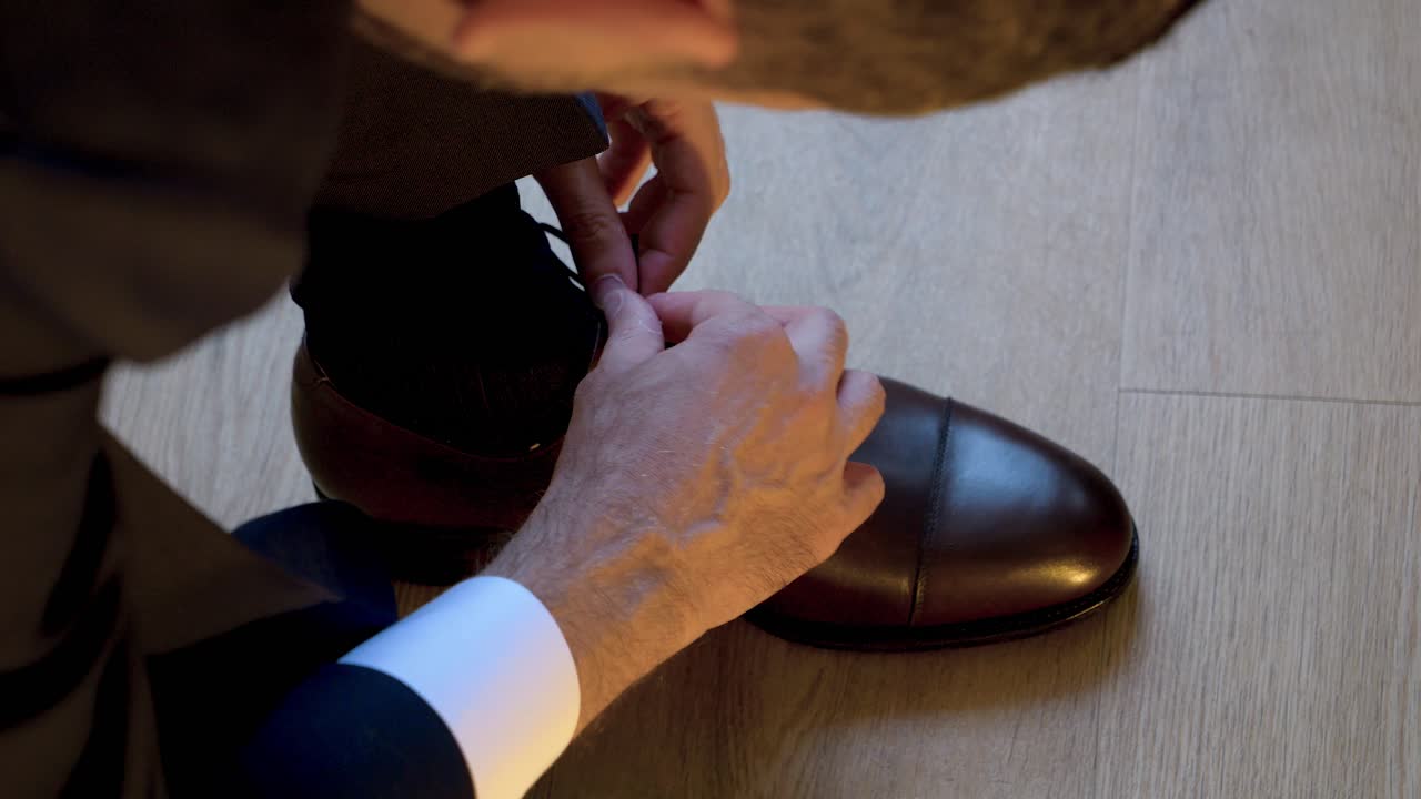 A man in a suit ties his shoelace on his luxurious black shoes