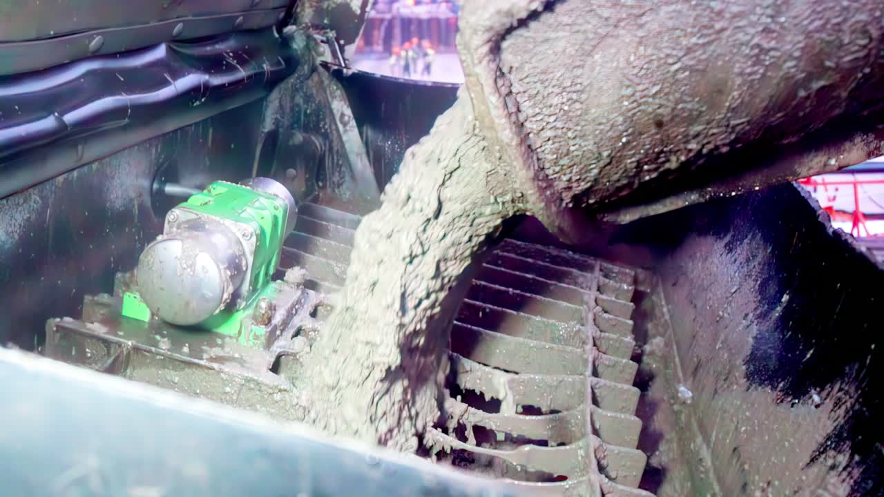 Nærbillede af tyk beton, der flyder fra en blander ned på en metalrist, med et kort kameratilbagetræk, før der bevæges ind i et ekstremt nærbillede af det flydende materiale