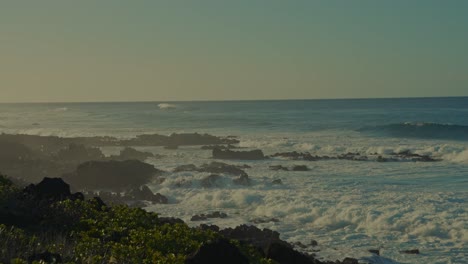 the white caps on the blue ocean waves gather at the shore along the island coast of kaena point on oahu, hawaii as the sun begins to set