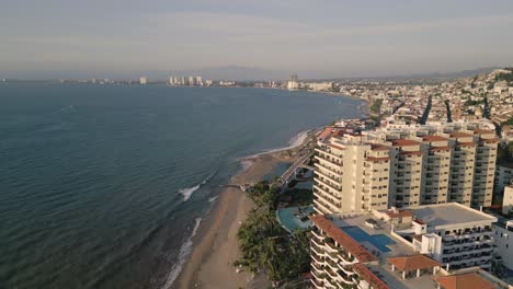 Drone-Aéreo-Vuela-Frente-A-La-Playa-Hoteles-En-Puerto-Vallarta-En-El-Paisaje-Marino-De-La-Playa-De-Verano-Mexicano,-Vibrante-Destino-De-Ciudad-Turística