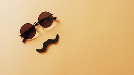 video of false moustache and round sunglasses on yellow background with copy space