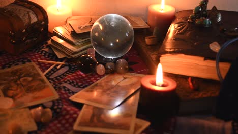 background of a fortune teller table covered with fabric, with crystal balls, stones, matches, cards, ancient books, rings and candles with flickering flames