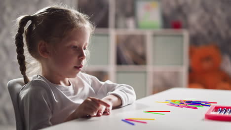 Schoolgirl-counts-aloud-sticks-solving-problem-at-lesson