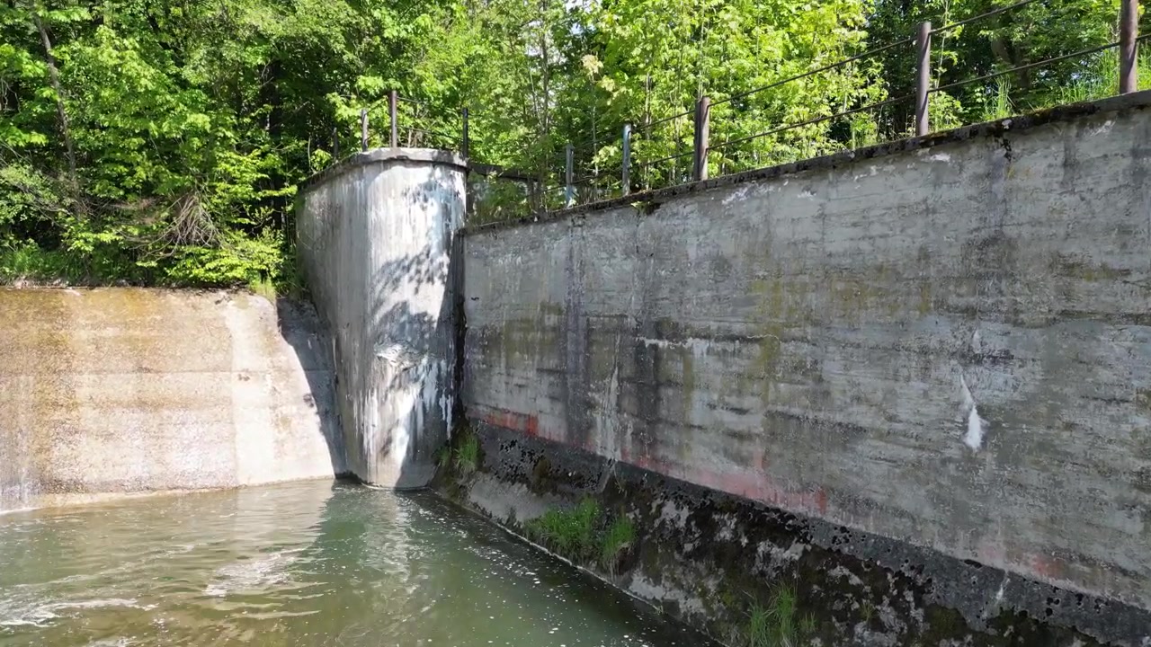 Vista aerea cinematografica del fiume Koszarawa con uno sfioratore d'acqua, acqua bianca a cascata, sponda rocciosa del fiume, foresta verde durante una soleggiata giornata estiva.