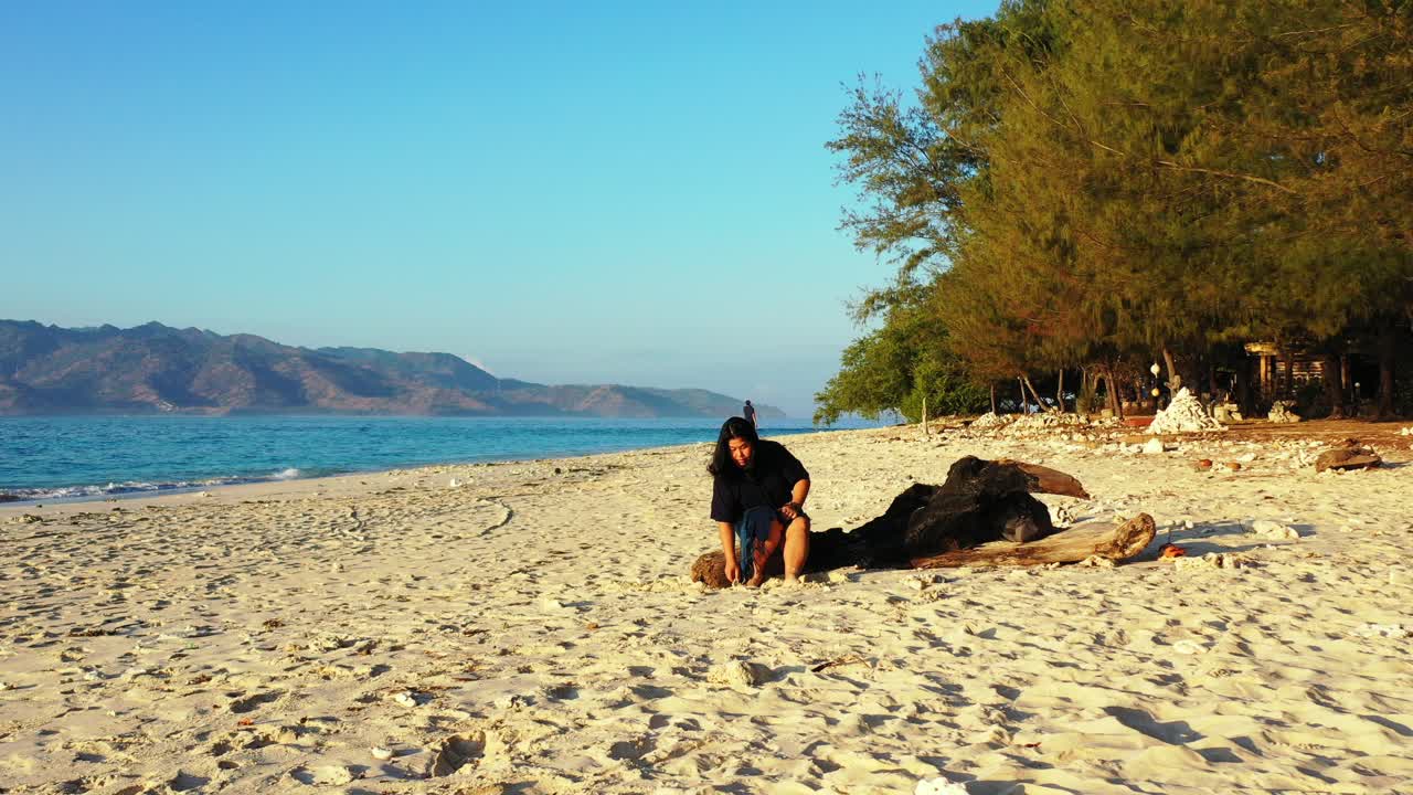 niña sentada en un baúl jugando con arena blanca de una playa exótica bañada por el mar azul que rodea la isla tropical en indonesia