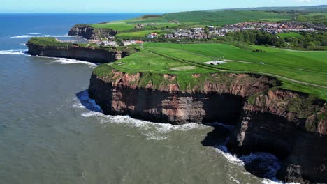 high drone view of north yorkshire coastline showing tall cliffs and multiple coves and textures as waves crashing from the ocean into the cliffside with birds flying around