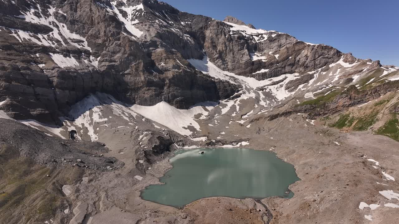 Aerial view of the Klausenpass in Kanton Uri, Switzerland, reveals the vast, alpine landscape with a small, serene glacial lake visible, nestled in the mountains