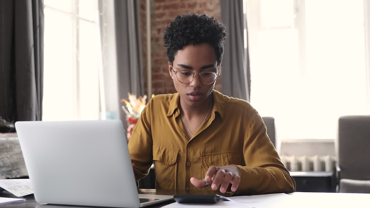 mujer africana revisando facturas domésticas, calcula resumen, hace pago en línea