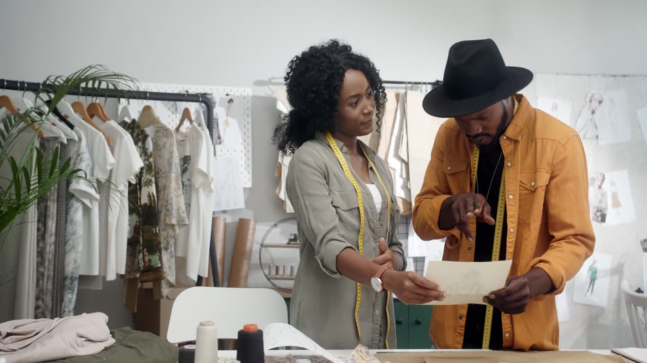 joven diseñadora mostrando un boceto de ropa a su colega diseñador masculino