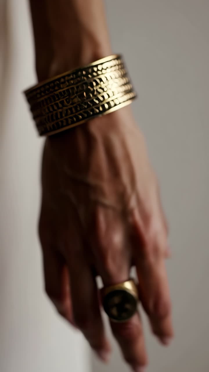 Close-up of a hand adorned with golden cuff bracelets and a ring