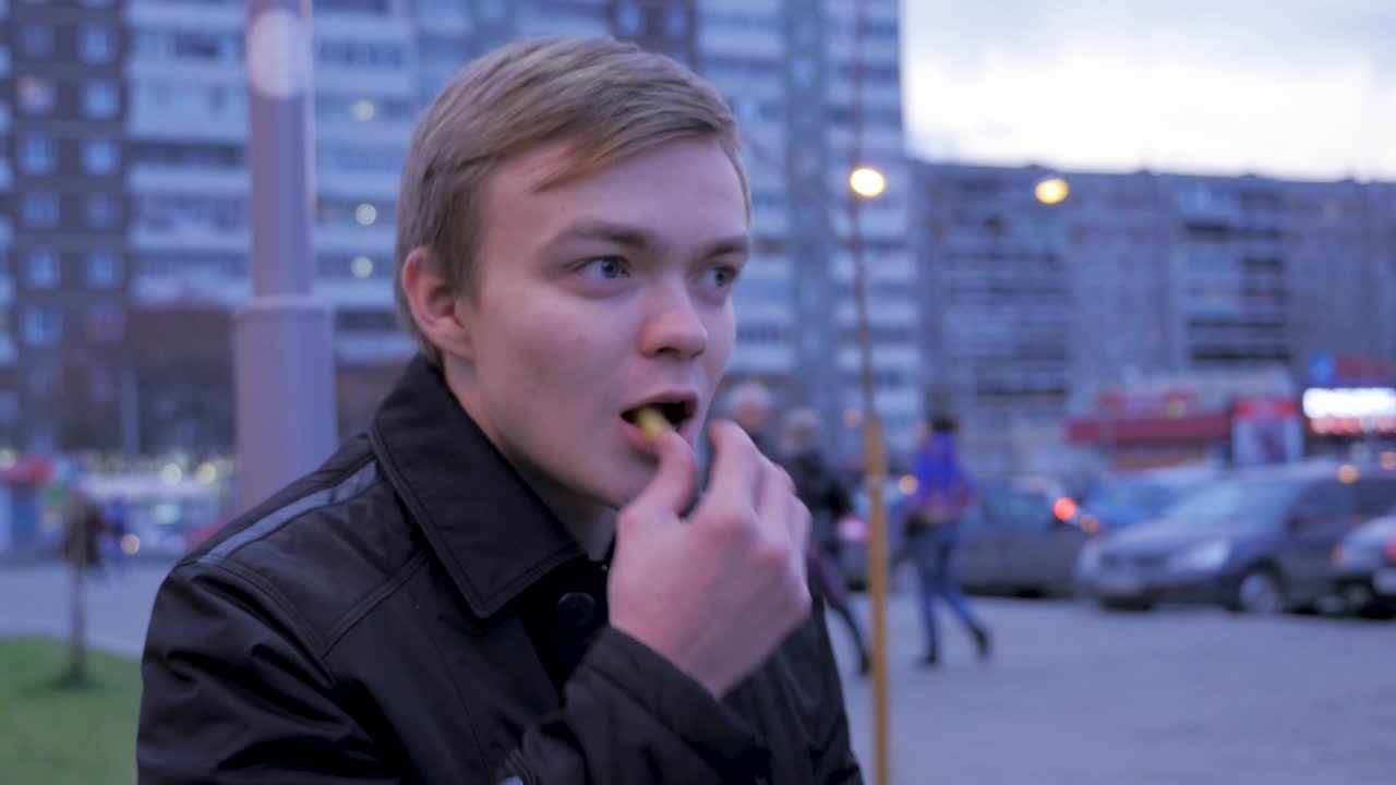 молодой человек ест на городской улице