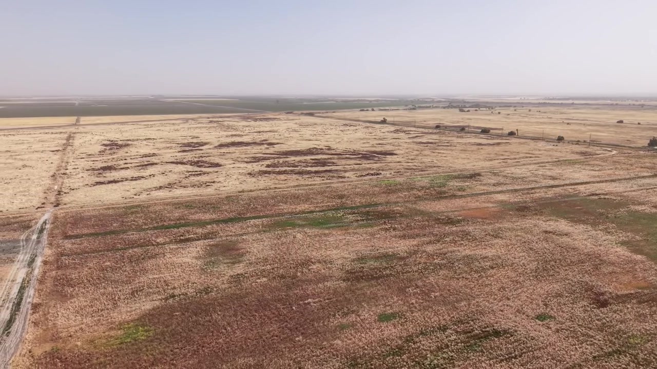 Riprese aeree con drone che sorvolano il paesaggio arido e secco che circonda il Lemoore College in California. Mostrando vasti campi e pianure sotto un cielo velato. Evidenziando le condizioni di siccità dello stato