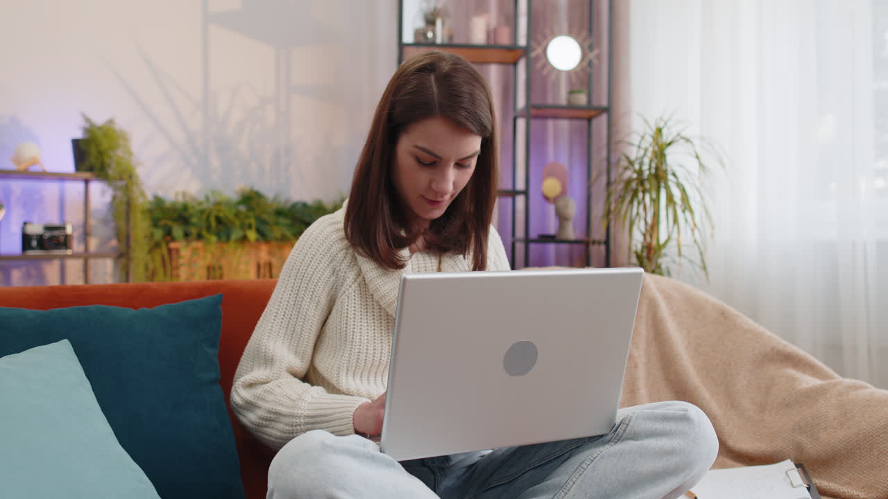 mujer joven independiente sentada en el sofá cerrando la computadora portátil después de terminar el trabajo en la habitación en casa