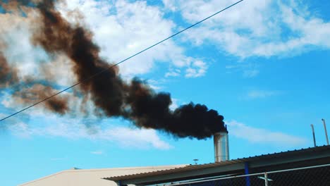 black smoke billowing out of steel chimney, blue sky background