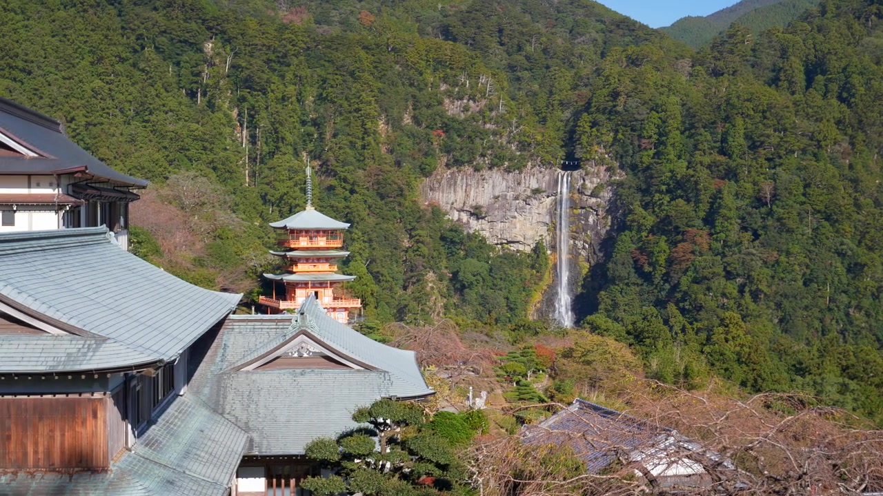 Wakayama, Jepang: Rekaman stok bergerak ke kiri dari kanan, menangkap Air Terjun Nachi dan Pagoda Tiga Tingkat Kuil Seigantoji. Tampilkan pemandangan indah landmark ikonik ini dalam satu video panorama.