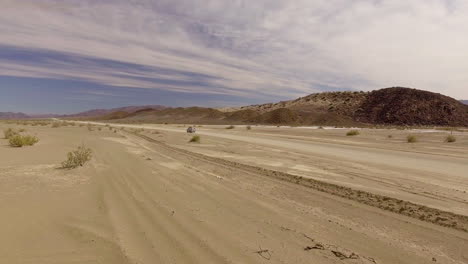 Aerial Pan of car driving past desert mountains on sandy road in African desert