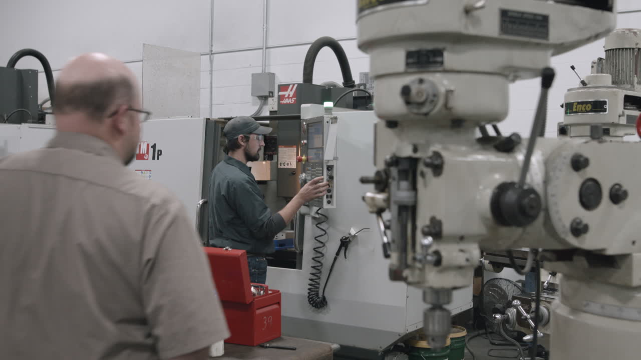 Trade school student operates a CNC drilling machine as his instructor observes