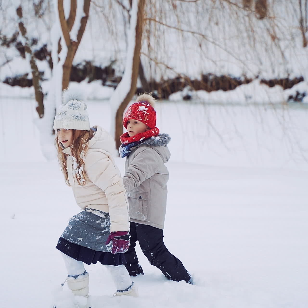 Curious children are walking together in a snowy background. Little boy and a girl spend a good time on the beautiful winter landscape outdoors. Slow motion.