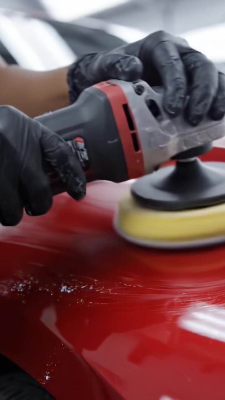 Um Técnico Especialista Polindo a Superfície de um Carro Vermelho para Alcançar um Brilho Perfeito e Realçar Sua Aparência Geral em um Ambiente Profissional de Detalhamento Automotivo