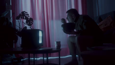 man eating snacks while watching tv at night
