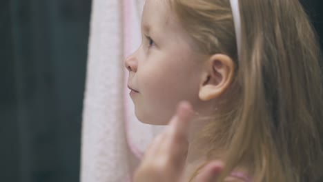 happy girl with long hair looks at mirror in light bathroom