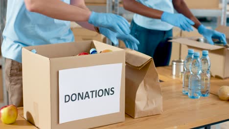 close-up view of volunteers hands packing box and giving bags with food and water to homeless people in charity warehouse