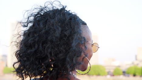 trendy young black woman in camisole and sunglasses walking over bridge, looking back and talking to camera, close up, follow shot