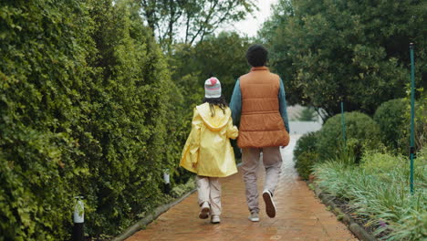 a father and daughter walk together down a path in a garden during a rainy day