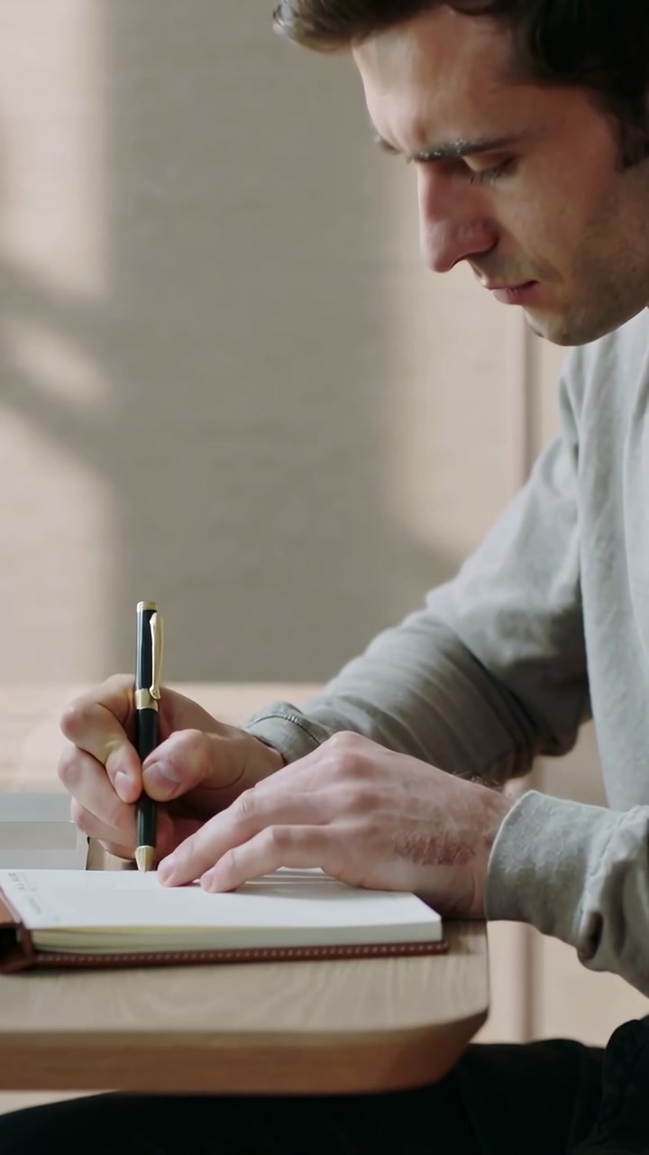 Vertical video: Opening notebook man gray-shirt writing at desk with pen turning page, copy space