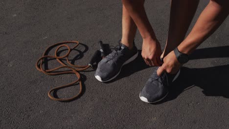 low section of african american man exercising in city with skipping rope, tying shoelaces in street