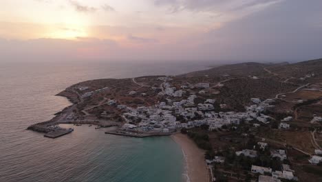 Häuser-Oberhalb-Des-Hafens-Neben-Dem-Strand-Mit-Klarem-Wasser-Bei-Sonnenuntergang-In-Donousa,-Griechenland,-Gebaut,-Luftumlaufbahn-Etablieren