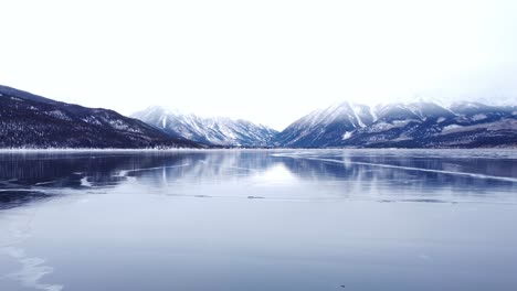 flying away from snow-capped mountains over frozen lake with cracks in the ice, aerial