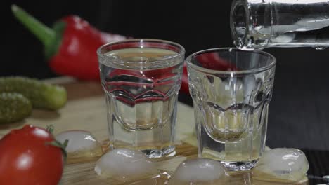 pour vodka from a bottle into shot glasses. man takes a glass with vodka