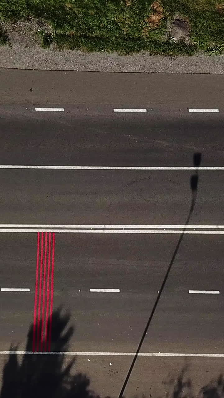 cars are passing on the road with red markings and with a pedestrian crossing. Aerial view. Camera motion to right Vertical video