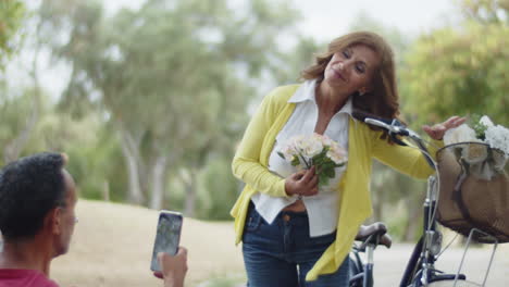 Front-view-of-man-taking-photo-of-his-wife-with-flowers-in-park