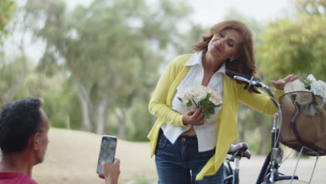 front view of man taking photo of his wife with flowers in park