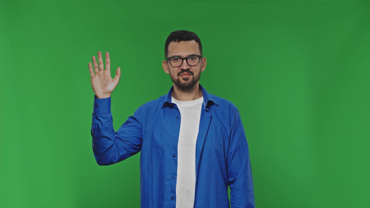 hombre agita su mano en la cámara mientras está de pie en el fondo de una llave de croma verde