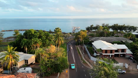 drone aerial of blue teal retro car down long winding road along coastline