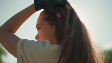 lady in black gloves gracefully adjusts her long hair, bathed in soft, warm sunlight that casts a natural glow around her, background of serene, blurred green trees and foliage