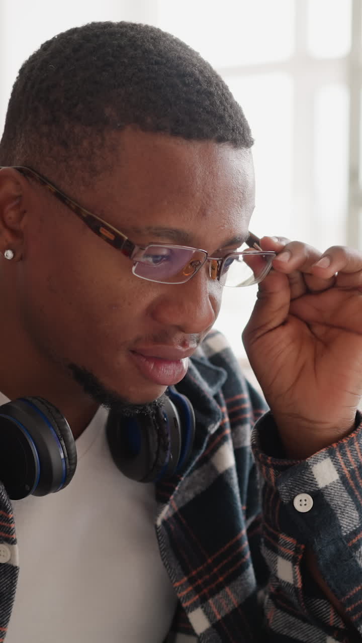 hombre con gafas trabaja en una computadora portátil en la biblioteca. joven negro con auriculares ajusta gafas sentado en la computadora en la sala pública. estudiante de tecnología