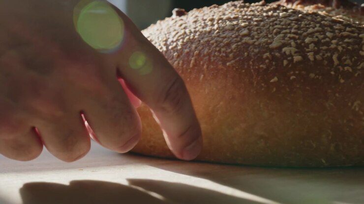 Reaching right hand sliding under round loaf on kitchen counter, preparing to lift in bright light