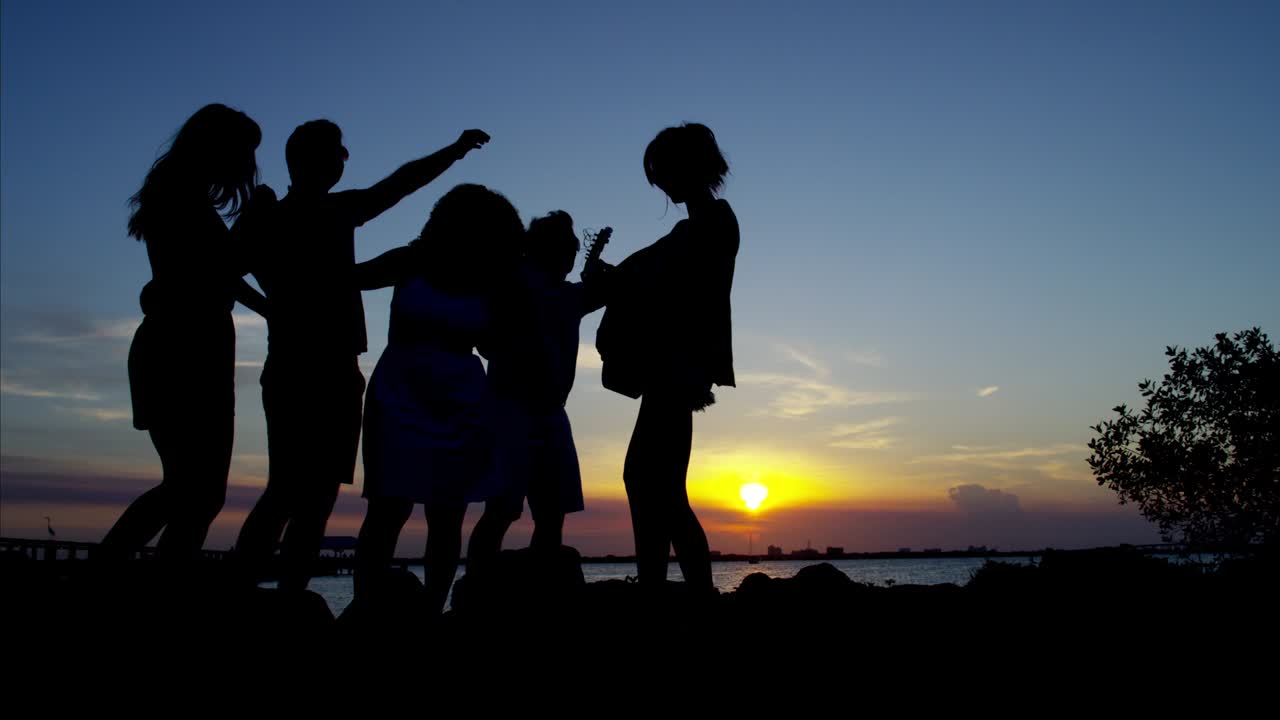 해가 지는 동안 해변 파티를 즐기는 친구들의 실루