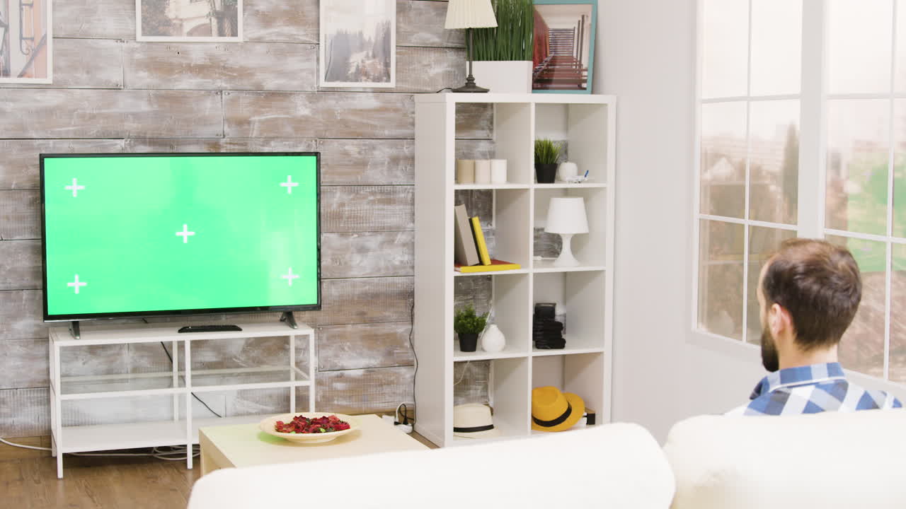 Man Watching TV with Green Screen in Modern Living Room