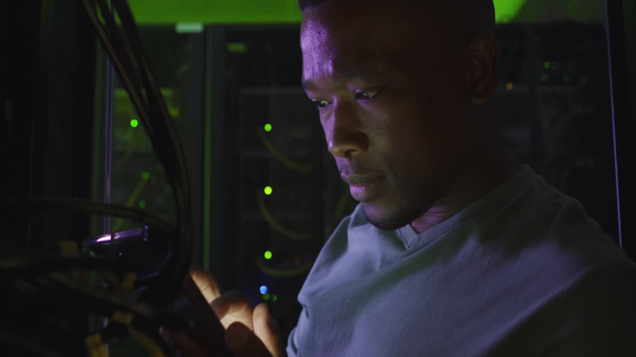 técnico informático afroamericano que usa un teléfono inteligente trabajando en una sala de servidores de negocios