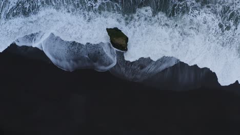 aerial top down shot of waves of ocean splashing against stapavík sea stack in iceland