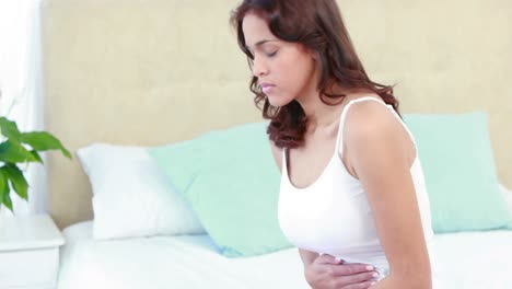 Woman-sitting-on-bed-with-stomach-pain-