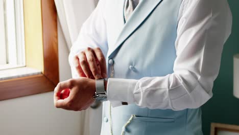 hombre ajustando el reloj de muñeca mientras lleva un chaleco de traje azul claro y una camisa blanca