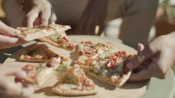 Primer plano de personas irreconocibles tomando porciones de pizza recién horneada de la mesa.